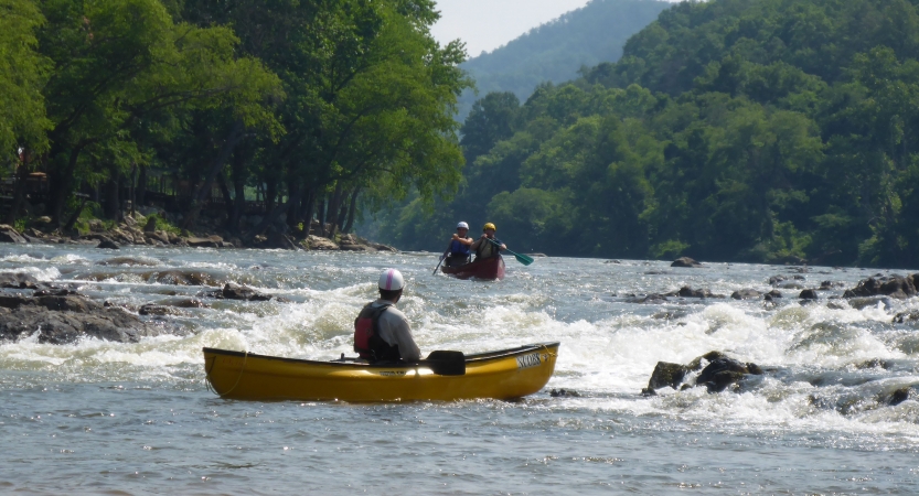 a person in a yellow canoe looks upriver at an oncoming canoe with two people in it 